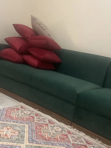 كنبة خضراء داكنة مع وسائد حمراء مميزة في منزل عميل